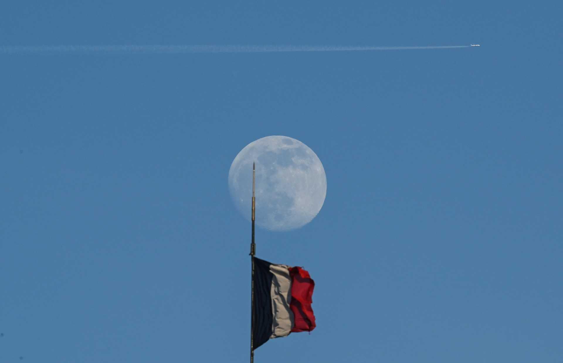 A plane flies over a French flag as the waxing gibbous moon rises in Paris on May 3. Photo: AFP