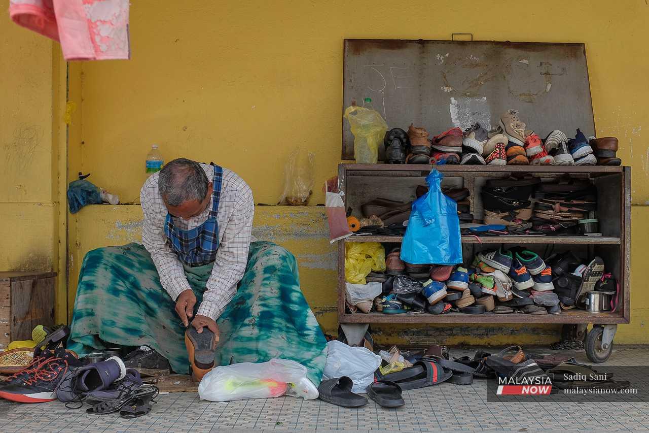 A cobbler mends a shoe as he waits for customers outside a shop. 