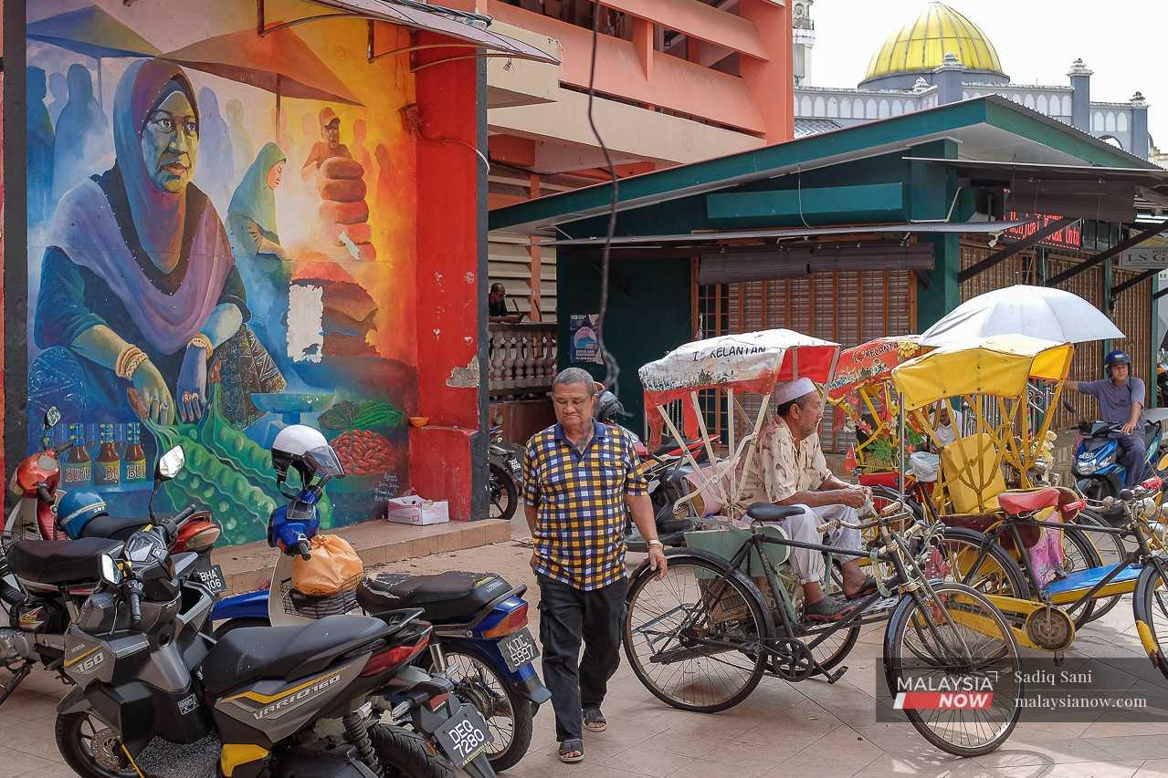 Outside, a man waits for customers at his rickshaw, near a wall decorated with a colourful mural. 
