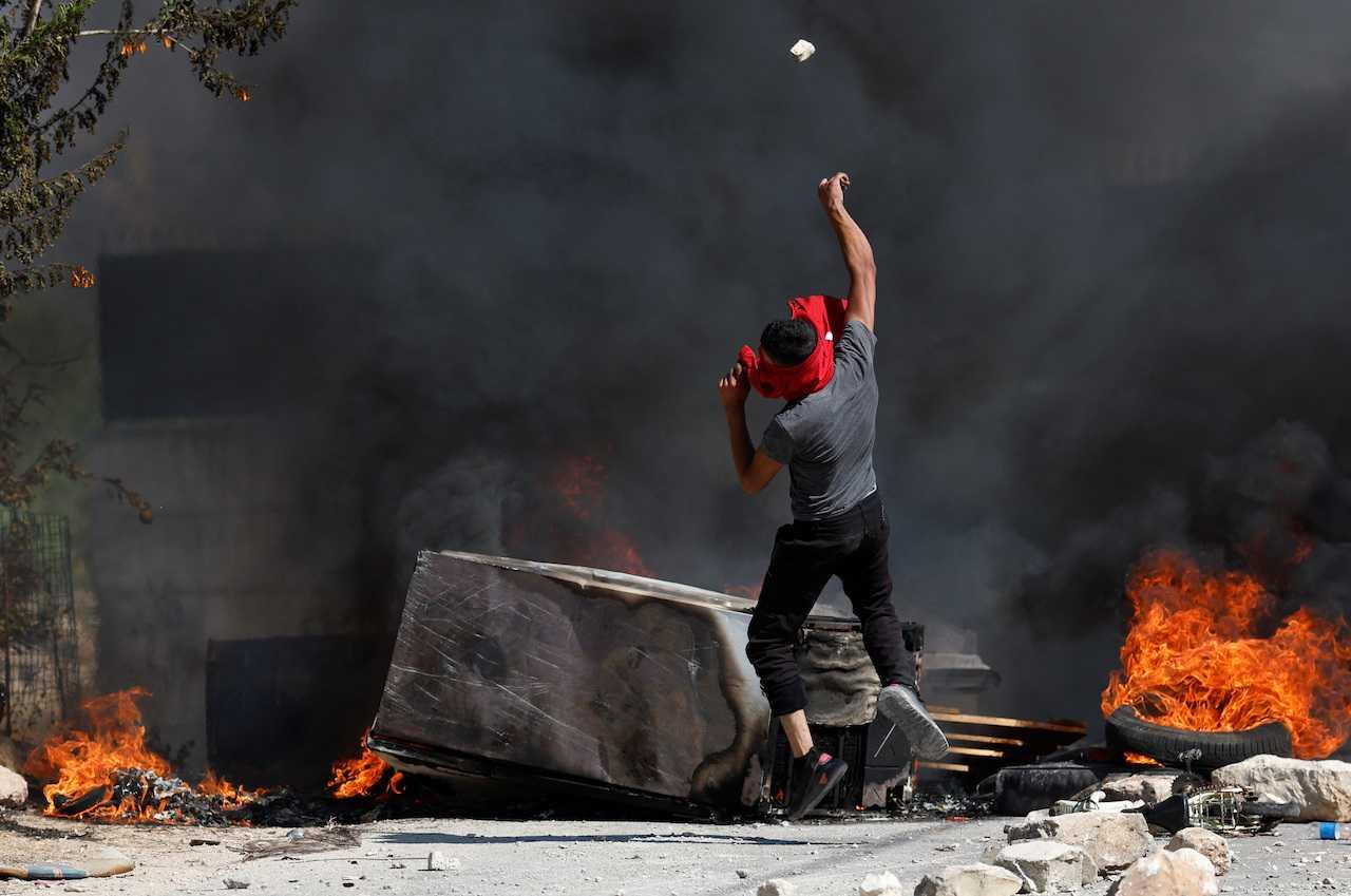 A Palestinian throws a stone during clashes with Israeli troops after Israeli settlers attack Umm Safa village near Ramallah, in the Israeli-occupied West Bank, June 24. Photo: Reuters