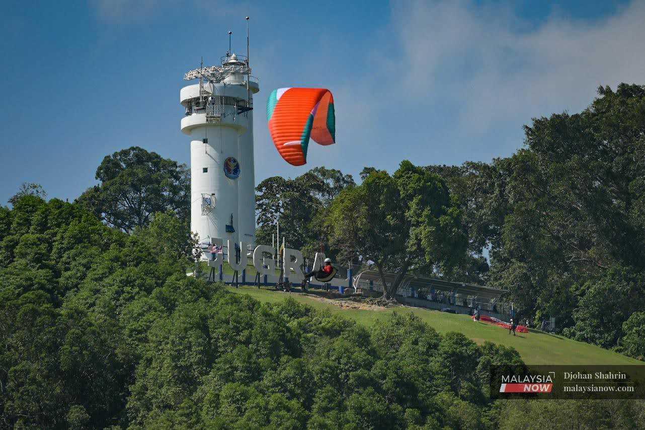 Seorang ‘paraglider’ atau luncur layar terbang sambil beberapa individu lain bersiap untuk penerbangan di atas bukit.