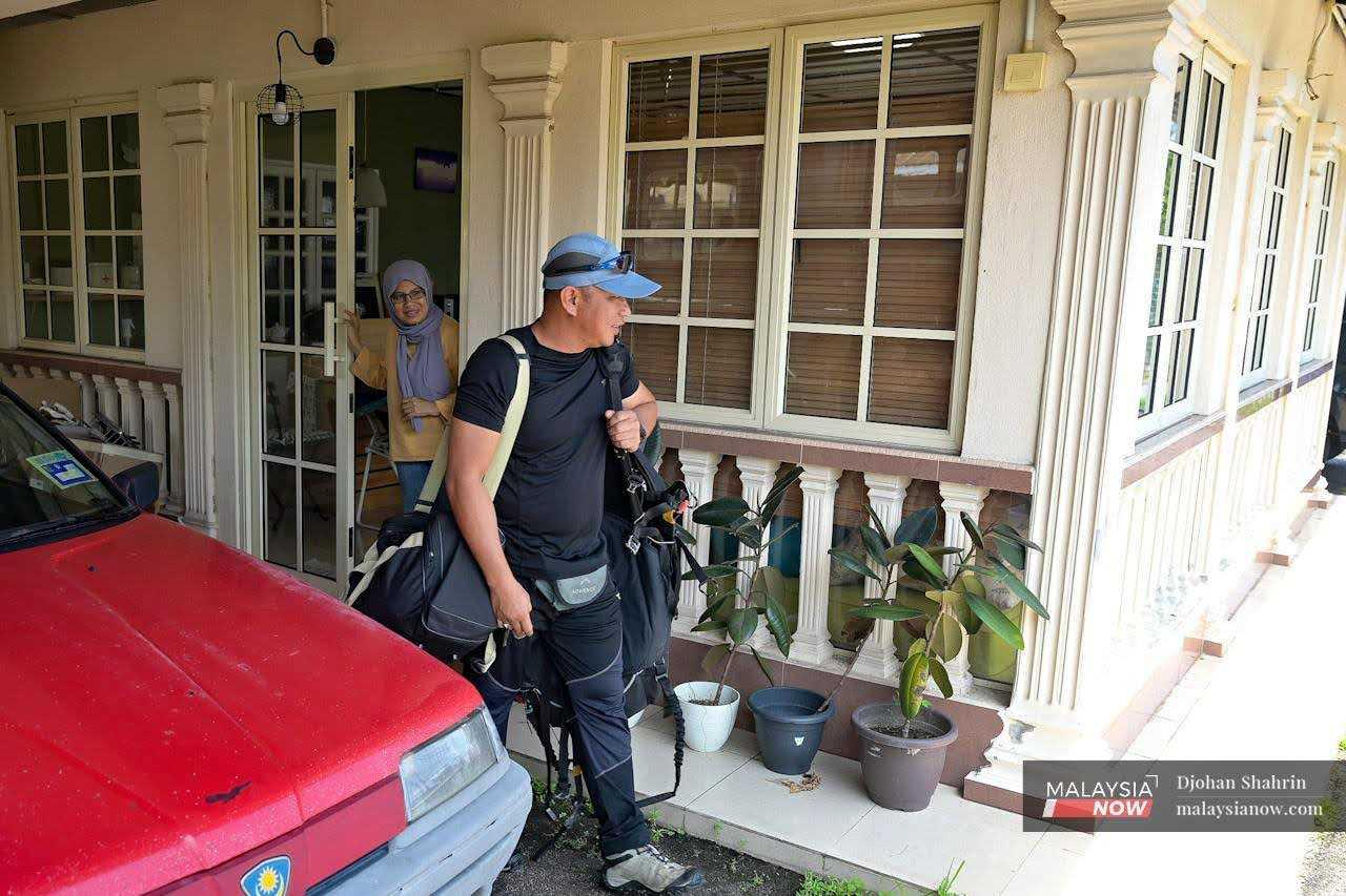 His wife sees him to the door as he leaves for work, carrying his equipment with him. 