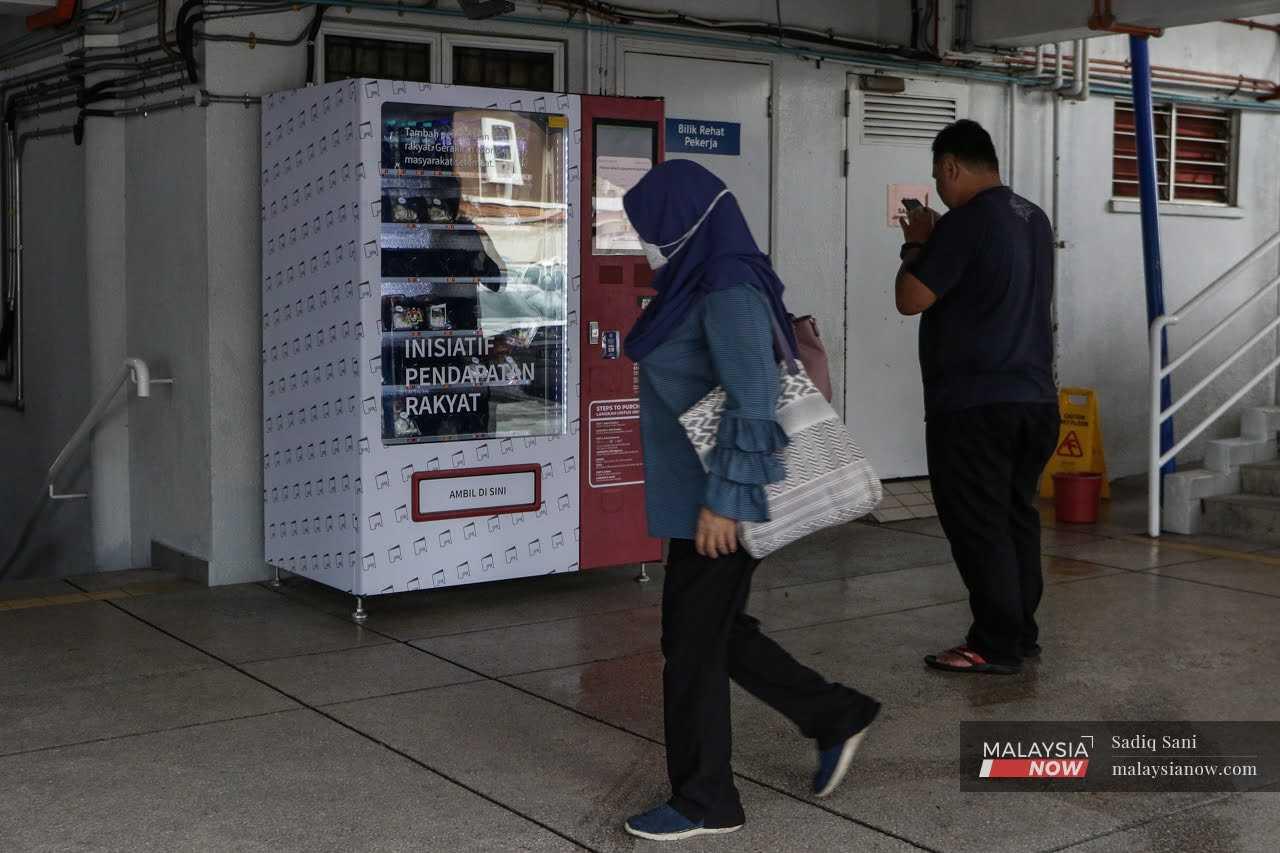 Seorang wanita berjalan melepasi mesin layan diri di Stesen LRT Cempaka yang disediakan Kementerian Ekonomi di bawah program Inisiatif Pendapatan Rakyat (IPR).