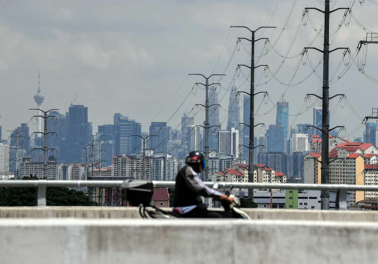 A motorcyclist passes transmission towers or electricity pylons in the capital city of Kuala Lumpur. Photo: Bernama
