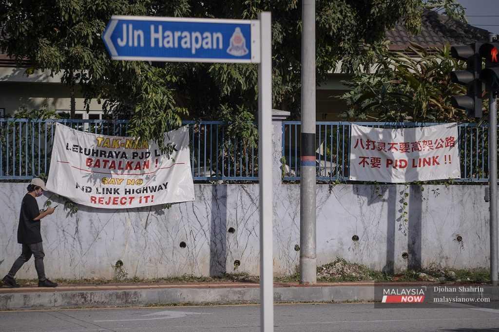 A man walks past banners in multiple languages objecting to the PJD Link along Jalan Harapan in Petaling Jaya.