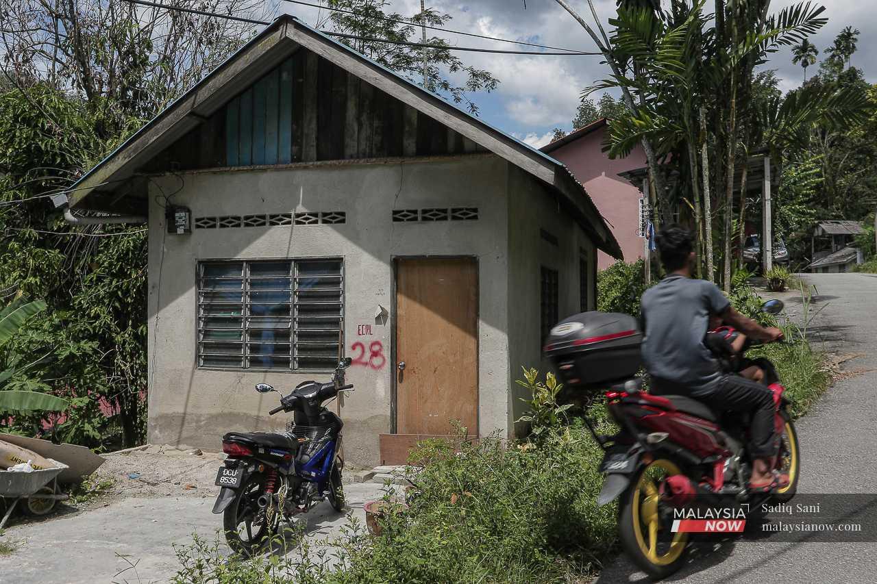 Seorang penunggang motosikal melalui sebuah rumah yang bertanda cat merah. 