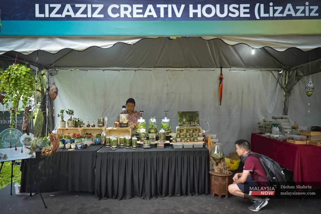 Aziz mans his expo booth selling terrariums at the festival as a customer examines the many items on display.