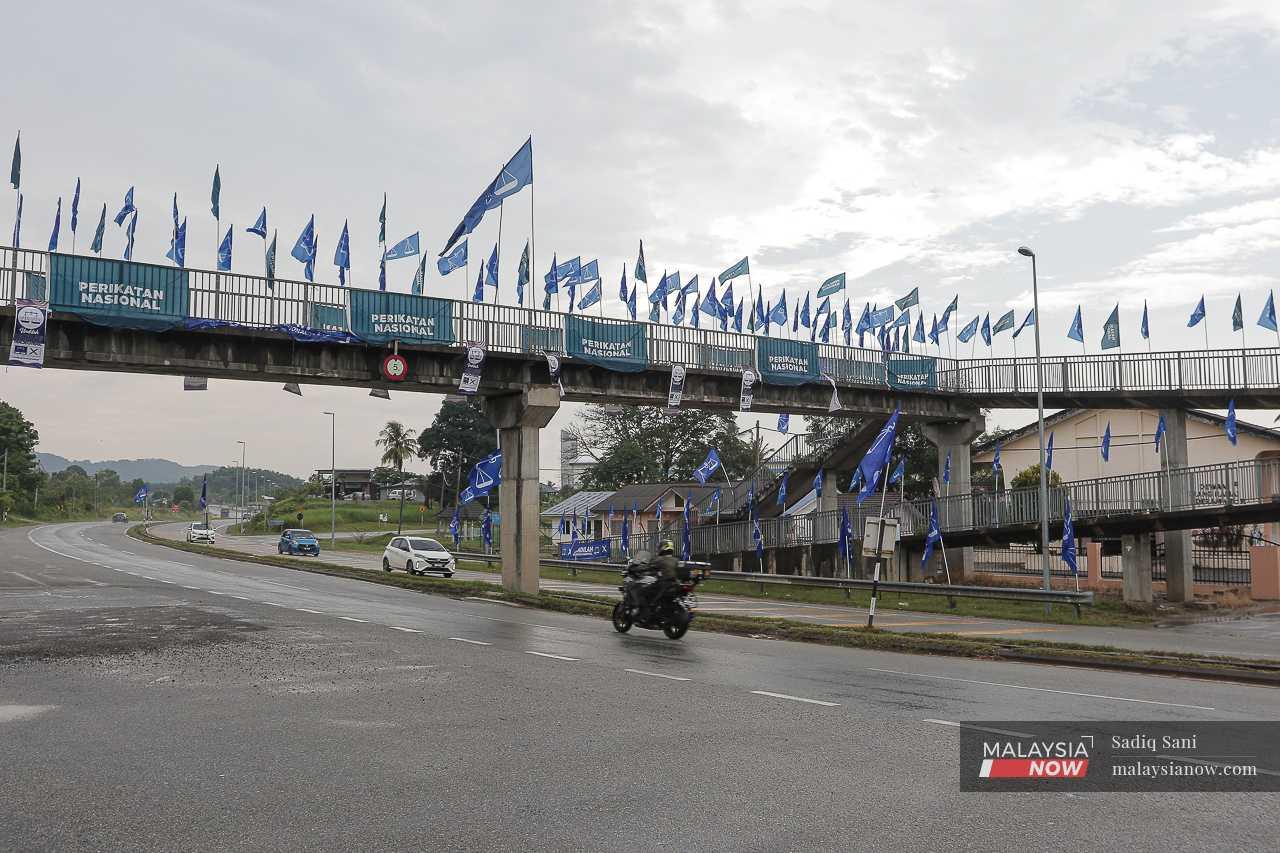 A motorcyclist passes beneath a flyover in Dengkil hung about with the flags of Perikatan Nasional and Barisan Nasional. 