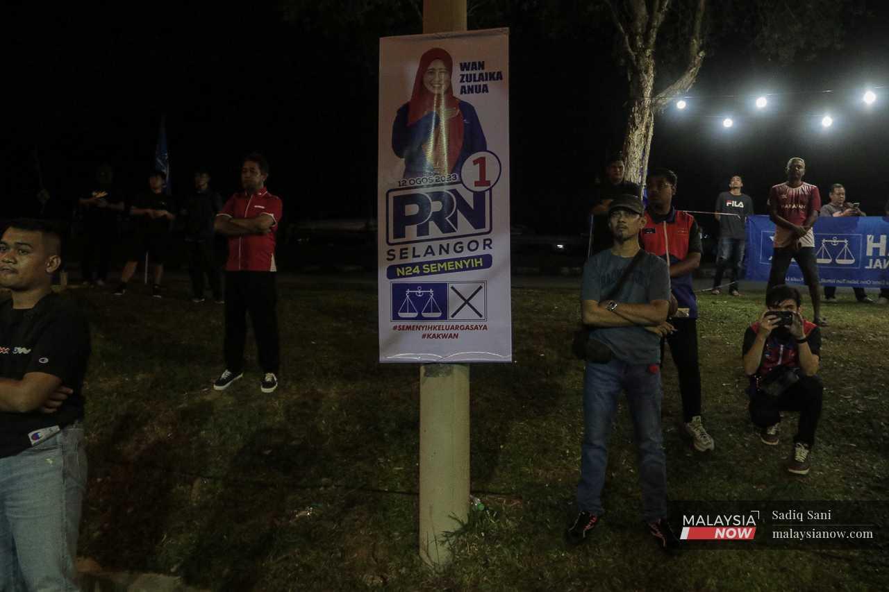 Supporters stand beside a poster featuring the Barisan Nasional candidate for Semenyih during a campaign event in Taman Tasik Bandar Kesuma.
