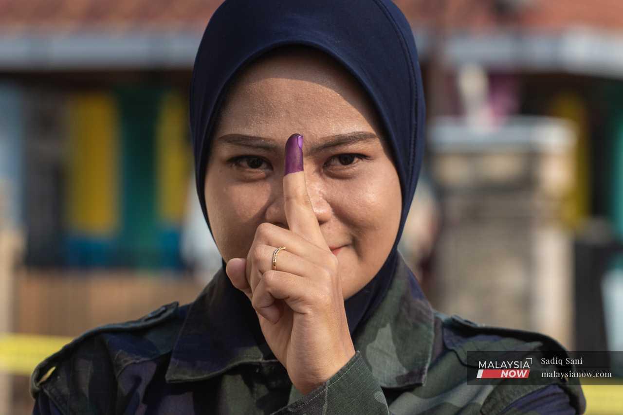 An officer holds up her ink-stained finger after casting her ballot paper.
