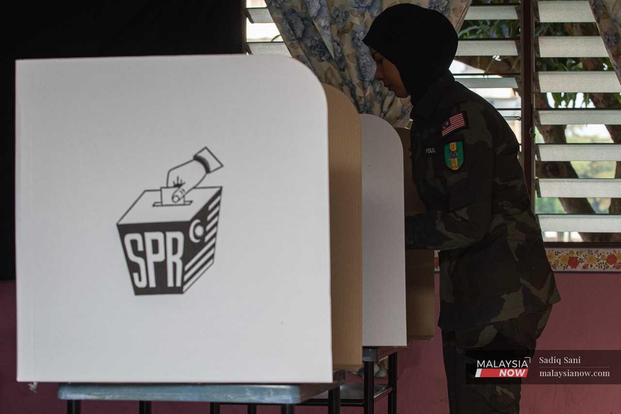 An officer stands at the polling booth to mark her ballot paper.