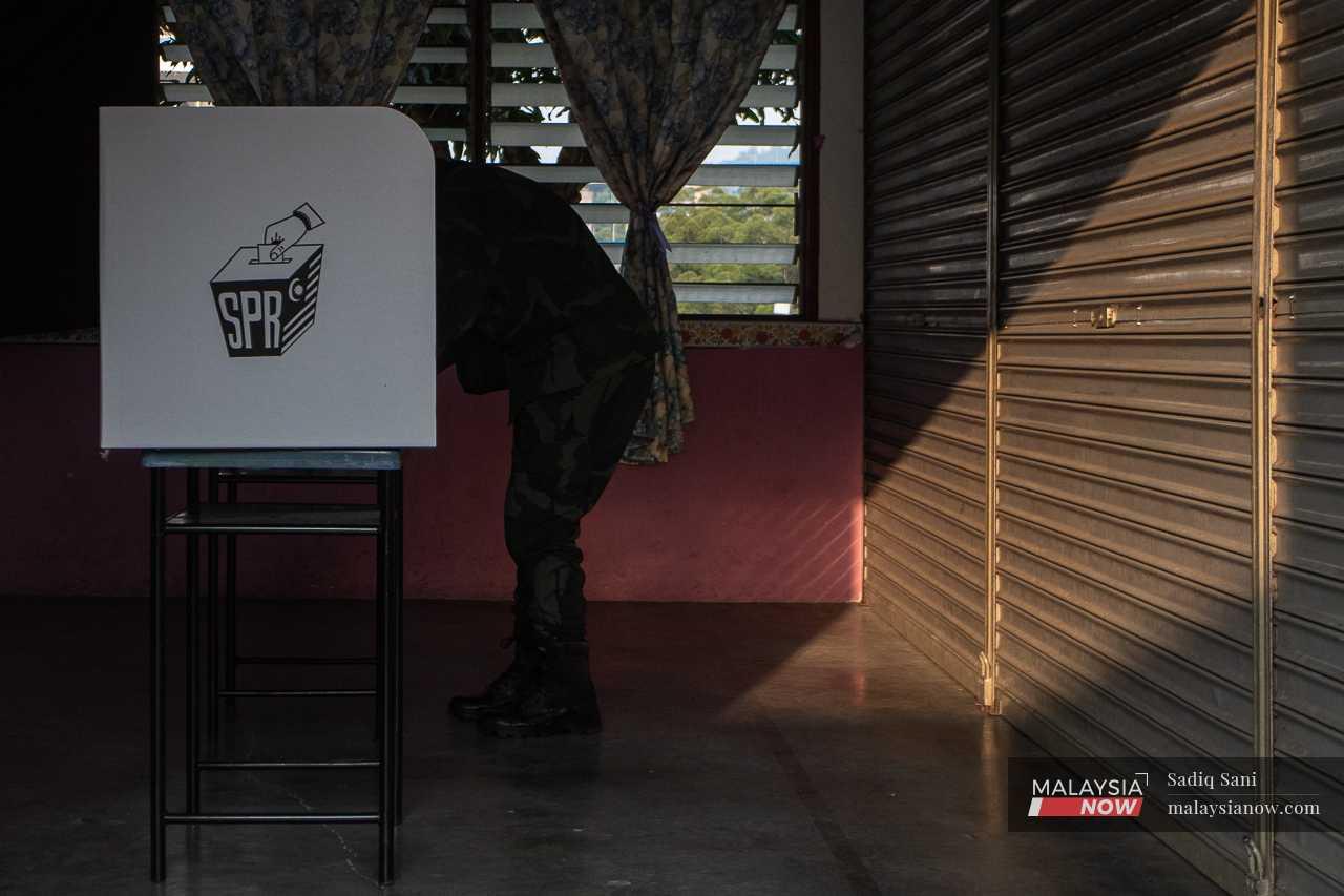 An officer bends over at a polling booth as he casts his ballot in early voting.