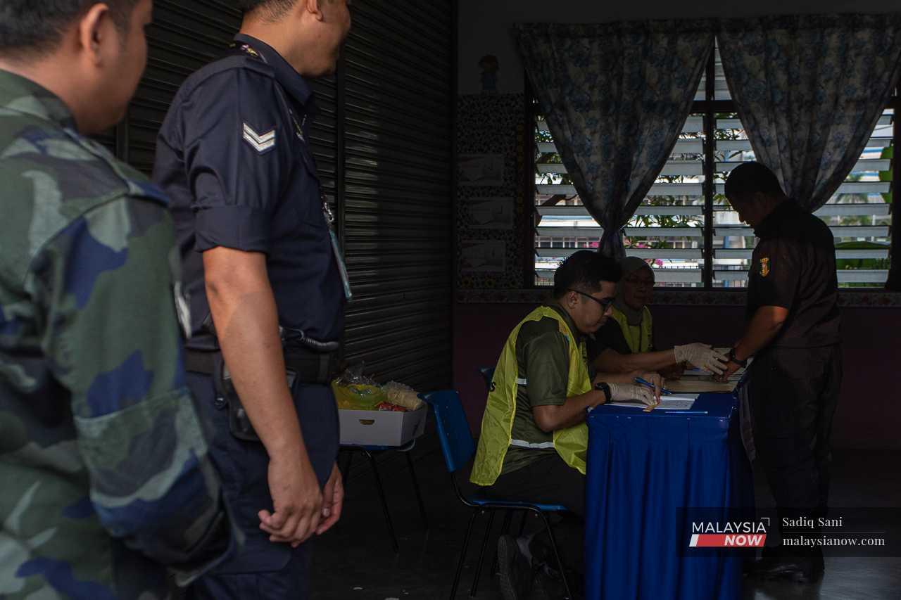 An officer dips his finger into a pot of indelible ink before casting his ballot as others wait for their turn outside the voting room.