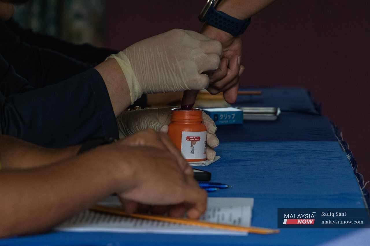 An officer dips his finger into a pot of indelible ink before casting his ballot at the Markas Briged Tengah Pasukan Gerakan Am early voting centre in Cheras.