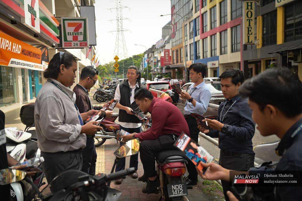 He distributes his campaign pamphlets to some people milling about at a motorcycle parking space during a walkabout.