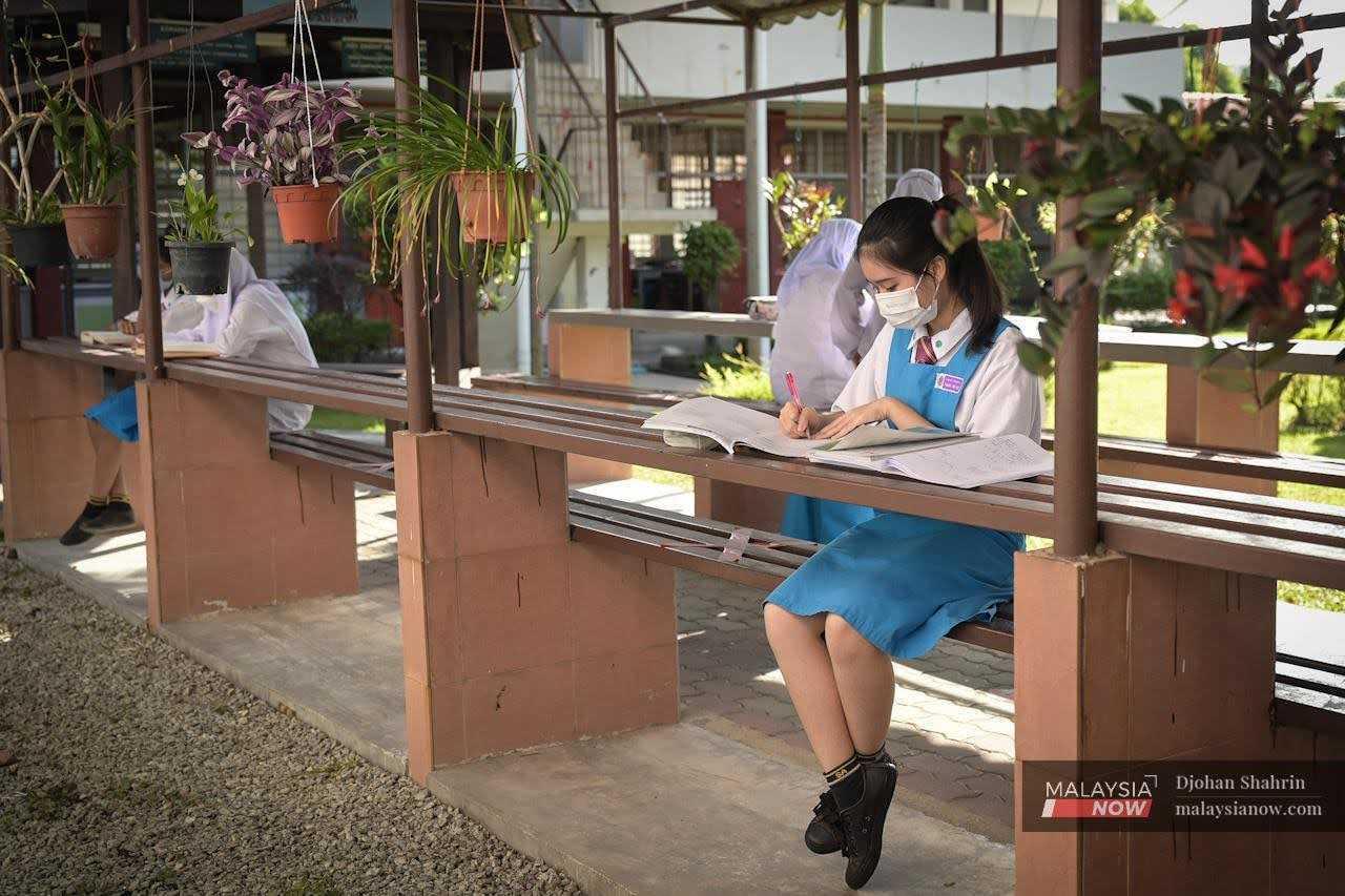 Seorang pelajar Sekolah Menengah Kebangsaan (P) Sri Aman menyiapkan tugasan di pondok rehat dengan lengkap memakai pelitup muka di Petaling Jaya, 16 Jun 2022.