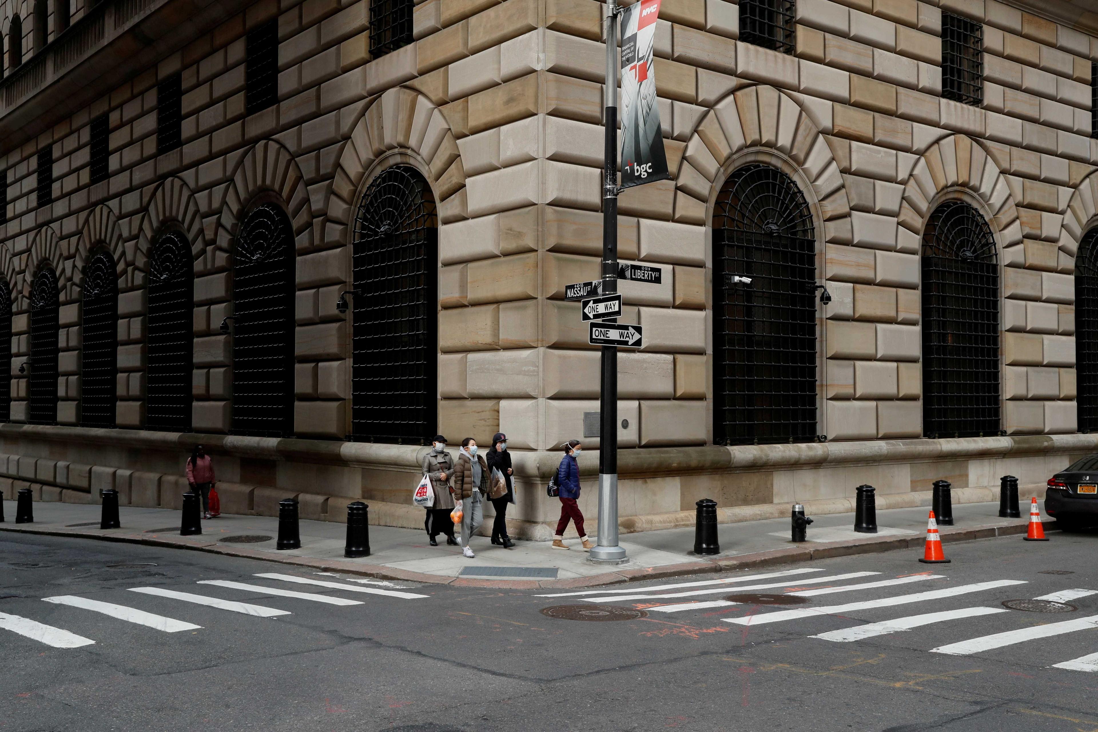 People walk wearing masks outside The Federal Reserve Bank of New York in New York City, US, March 18, 2020. Photo: Reuters