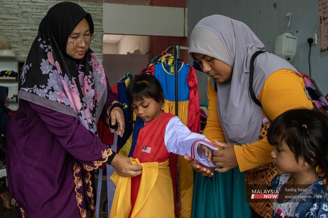 Helmaliza helps a customer's daughter put on the Tun Fatimah costume, which is part of her Jalur Gemilang collection.