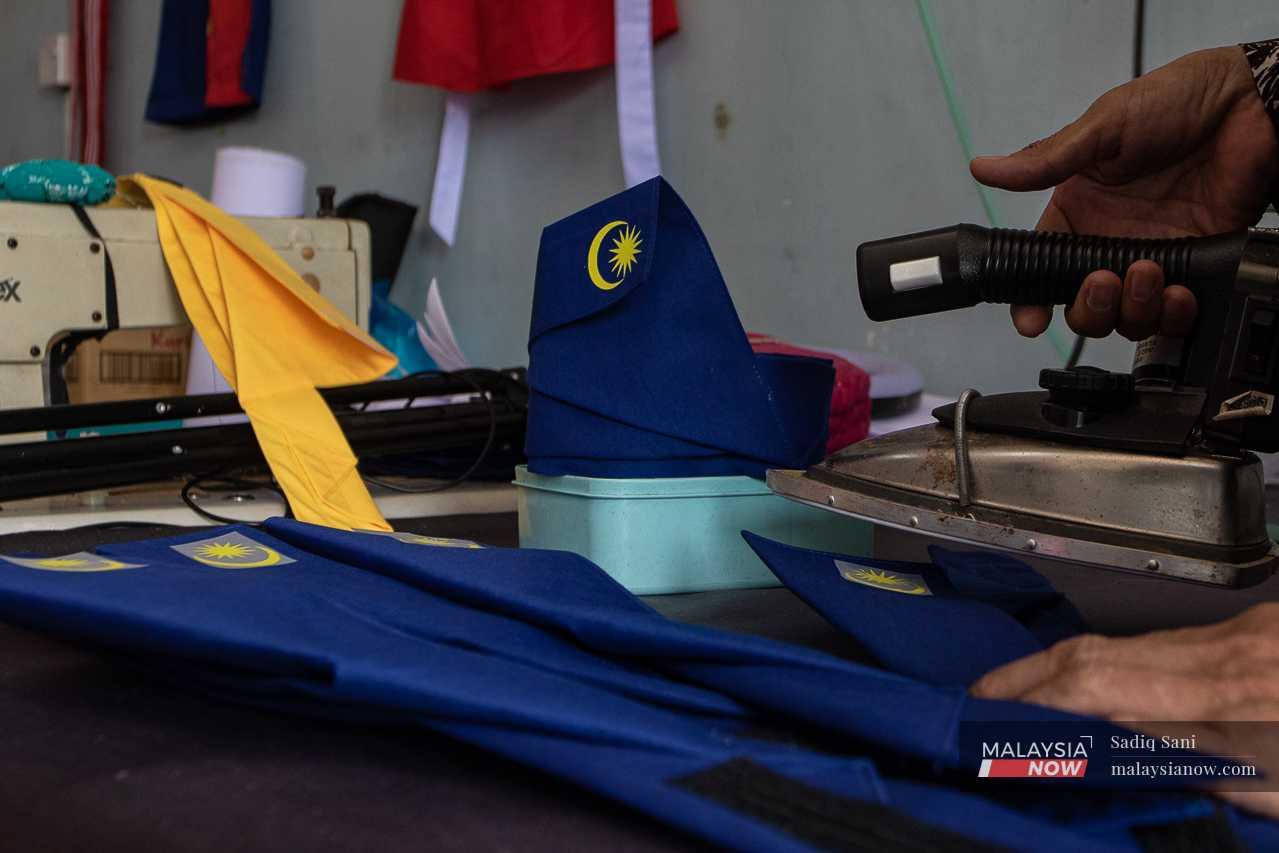 As Helmaliza sews, her assistant affixes a Jalur Gemilang logo sticker onto a traditional Malay headgear known as tengkolok.