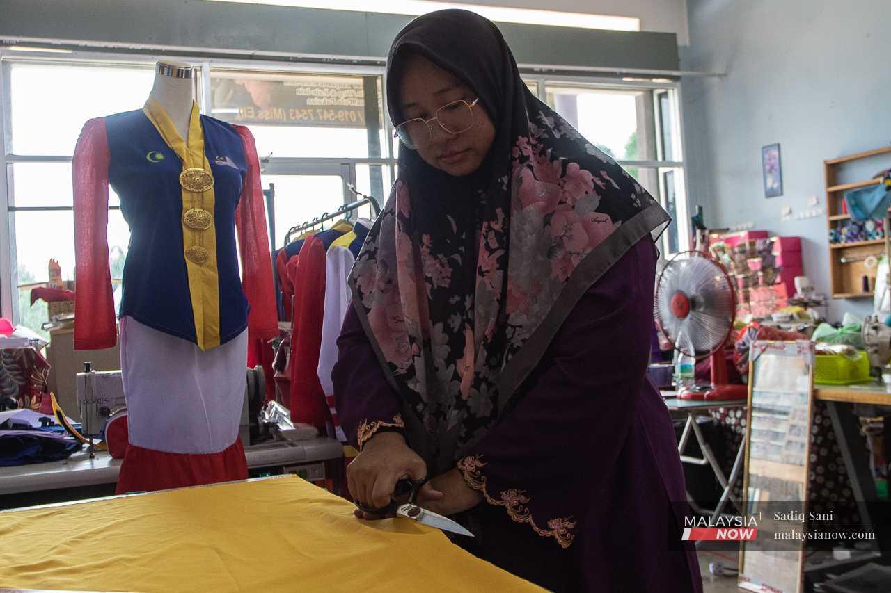 The 41-year-old skillfully cuts a piece of yellow fabric to create a matching scarf for her Jalur Gemilang kebaya collection.