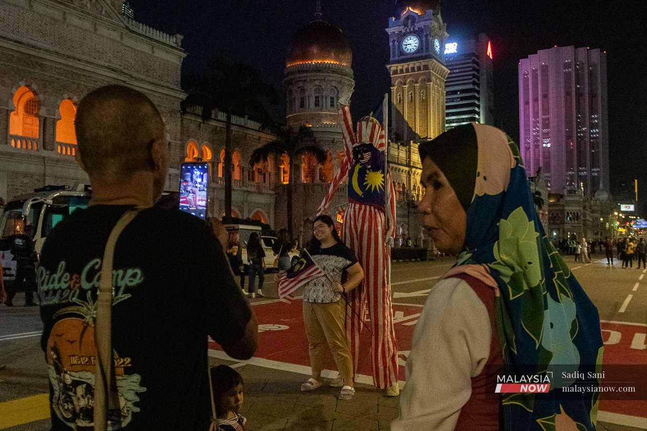 A woman poses for a picture with a man wearing a Jalur Gemilang costume at Dataran Merdeka. 