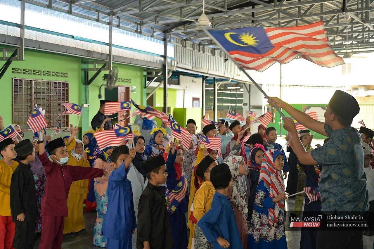 Students follow their teacher in waving the Jalur Gemilang at Sekolah Kafa Integrasi Islahiah Kampung Tasik Tambahan in Ampang. 