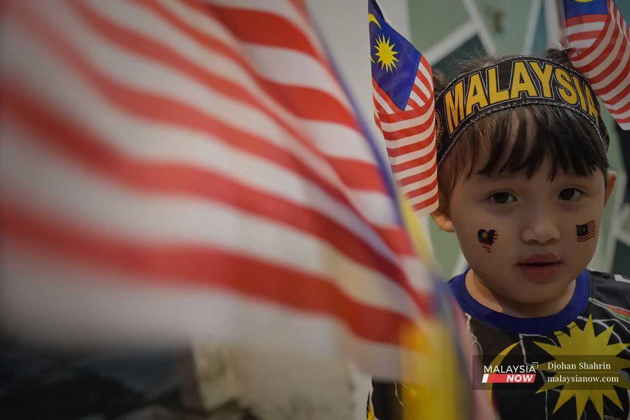 A girl festooned with flags and with Jalur Gemilang stickers on her face poses for a shot.