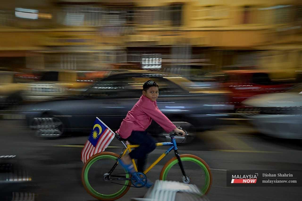 A boy looks over his shoulder as he cycles with a flag attached to his bicycle in Kampung Pandan. 
