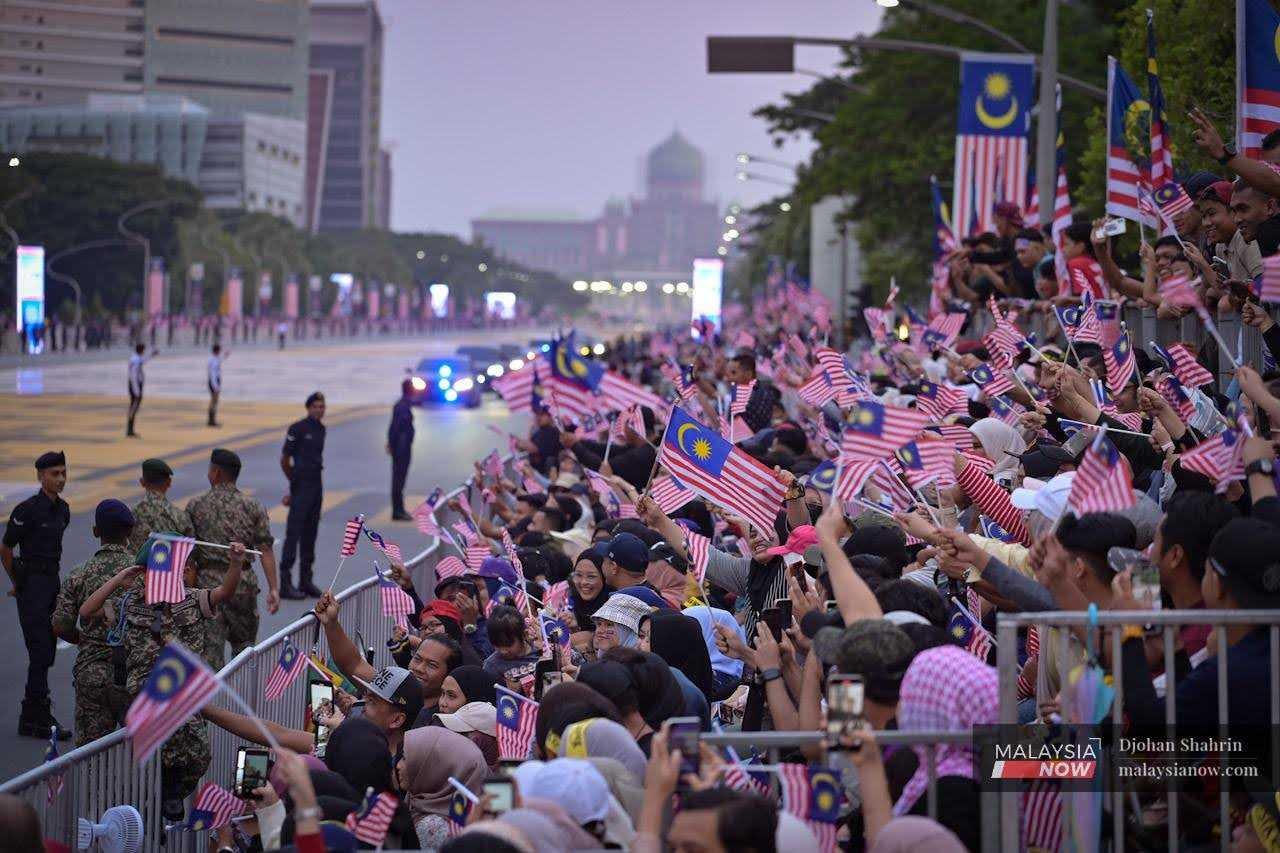 The crowd waves flags as they wait for the parade to begin at Dataran Putrajaya, Aug 31. 
