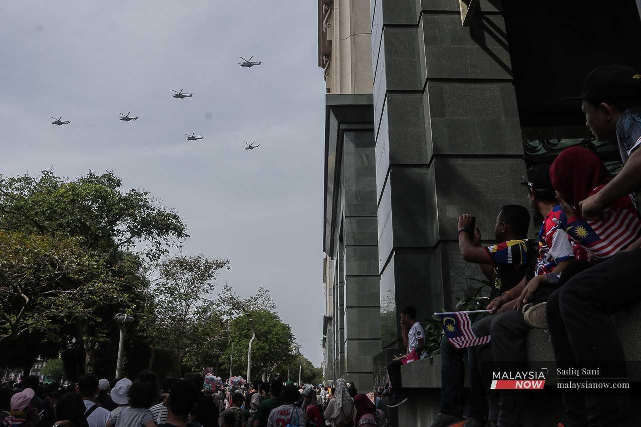 Helicopters fly past Dataran Putrajaya as the crowd watches from below.