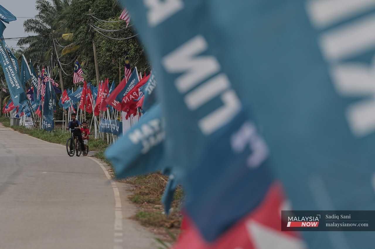 Children cycle along a road decorated with Perikatan Nasional and Pakatan Harapan flags in Kampung Bukit Batu, Simpang Jeram.