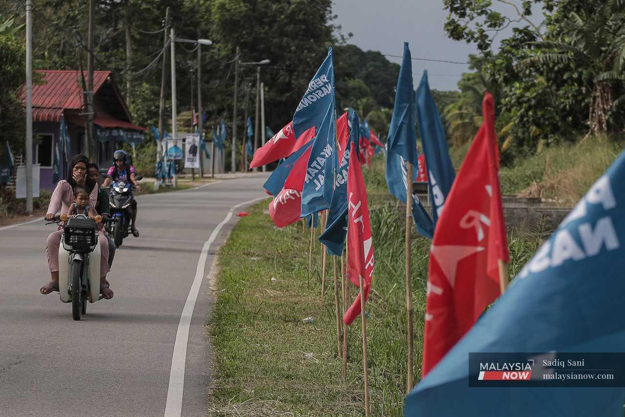 Seorang penunggang motosikal melintasi barisan bendera Perikatan Nasional dan Pakatan Harapan yang dipacak di tepi jalan menjelang Pilihan Raya Kecil Simpang Jeram.