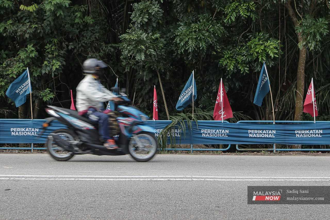 Seorang penunggang motosikal melintasi barisan bendera Perikatan Nasional dan Pakatan Harapan menjelang pilihan raya kecil Simpang Jeram di Johor.