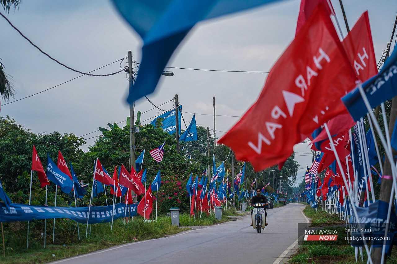 Penunggang motosikal menunggang melintasi deretan bendera Perikatan Nasional dan Pakatan Harapan di Simpang Jeram semasa Pilihan Raya Kecil Simpang Jeram pada 5 September.