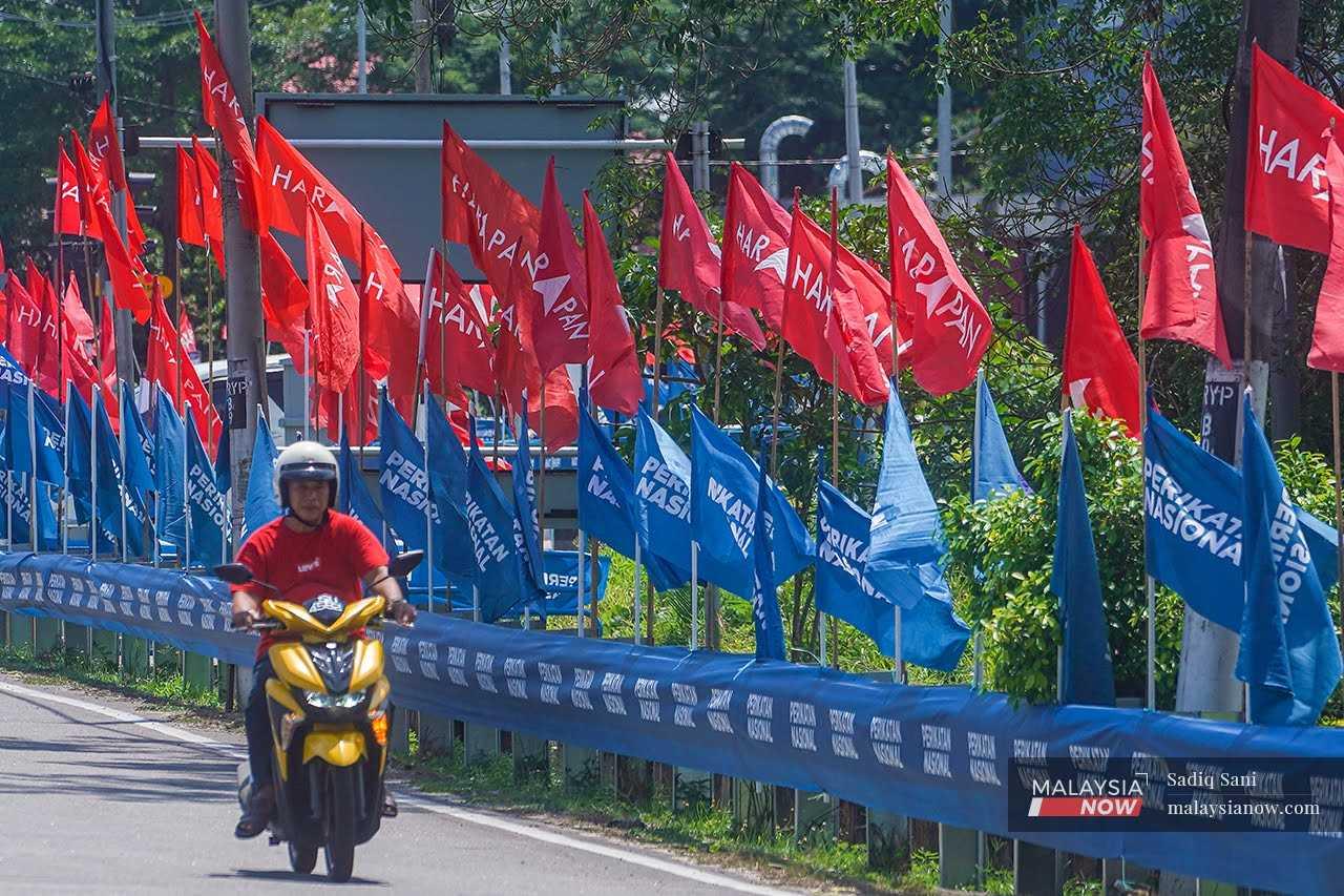 A motorcyclist rides past a row of Perikatan Nasional and Pakatan Harapan flags in Simpang Jeram.