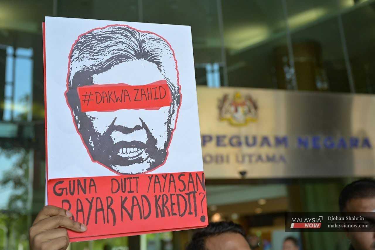A placard featuring a graphic of Deputy Prime Minister Ahmad Zahid Hamidi is held up outside the Attorney-General's Chambers in Putrajaya as Muda and Parti Sosialis Malaysia deliver a memorandum of protest against the decision to discharge him. 