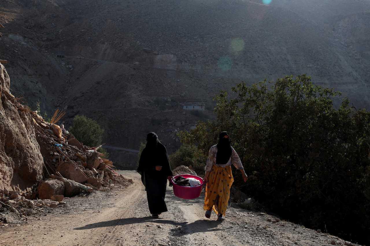 Two women walk on a hill as they help each other carry a heavy bag in the village of Tikht following the aftermath of a deadly earthquake in Morocco, Sept 14. Photo: Reuters