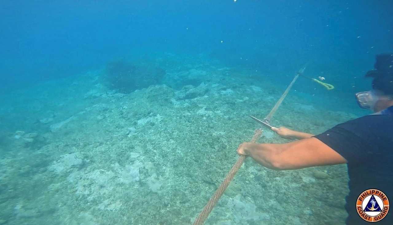 A Philippine Coast Guard personnel cuts the rope connecting a floating barrier that was installed near the Scarborough Shoal in the South China Sea, in an undated handout photo released on Sept 25. Photo: Reuters