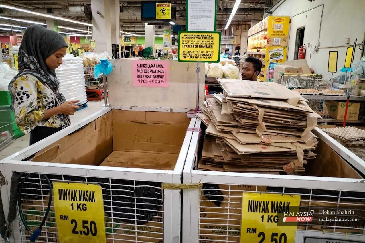 A woman stands next to an empty rack meant for 1kg packs of subsidised cooking oil at a supermarket in Taman Kuchai, Kuala Lumpur.