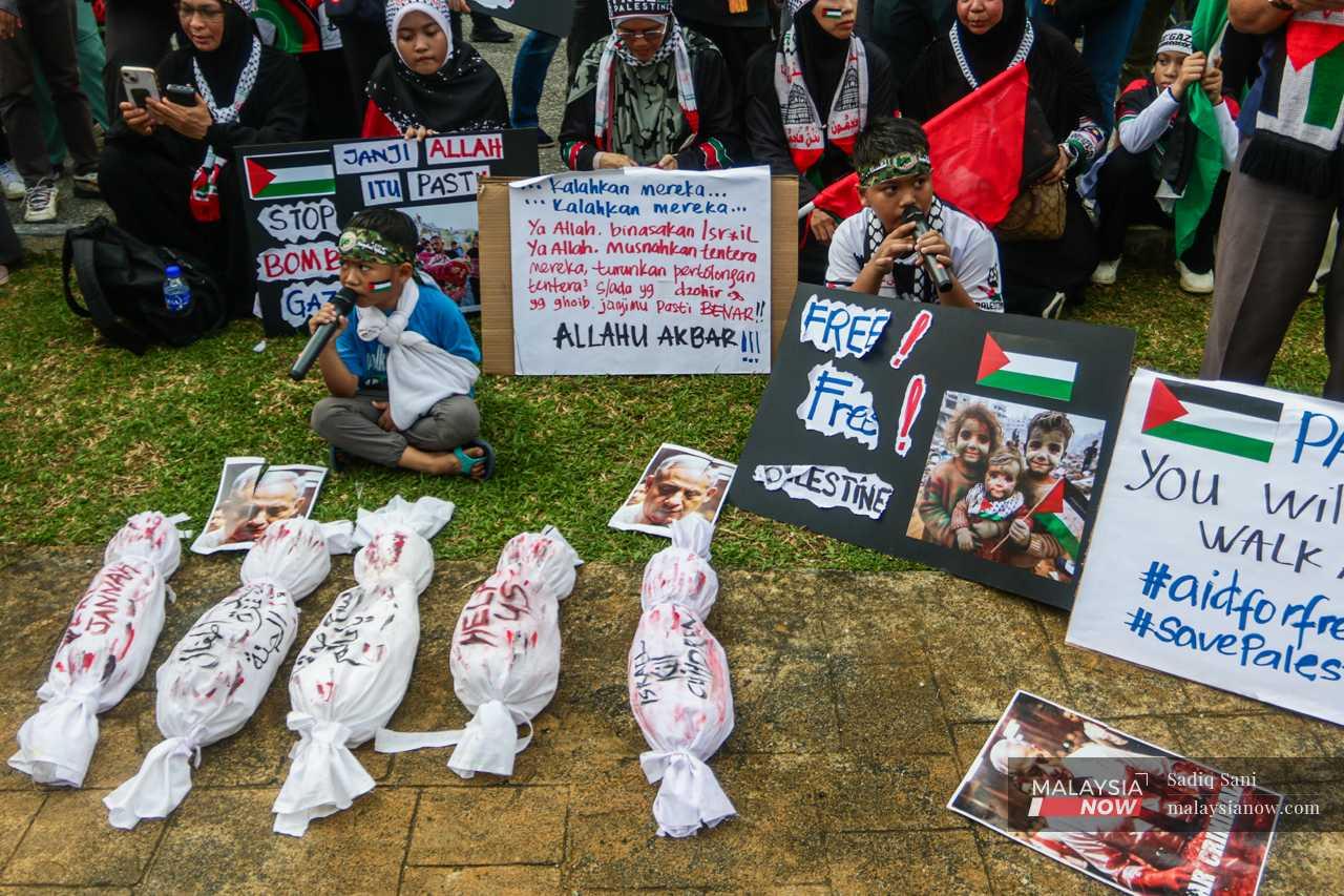 Mock body bags representing children killed in Israel's bombardment of Gaza lie on the road, accompanied by placards and banners, one of which is a supplication for the destruction of Israel.