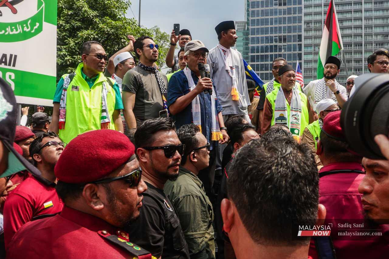 Several leaders from the opposition Perikatan Nasional lead the the crowd protesting outside the US embassy in Jalan Tun Razak, Kuala Lumpur, as members of PAS' security brigade stand by.