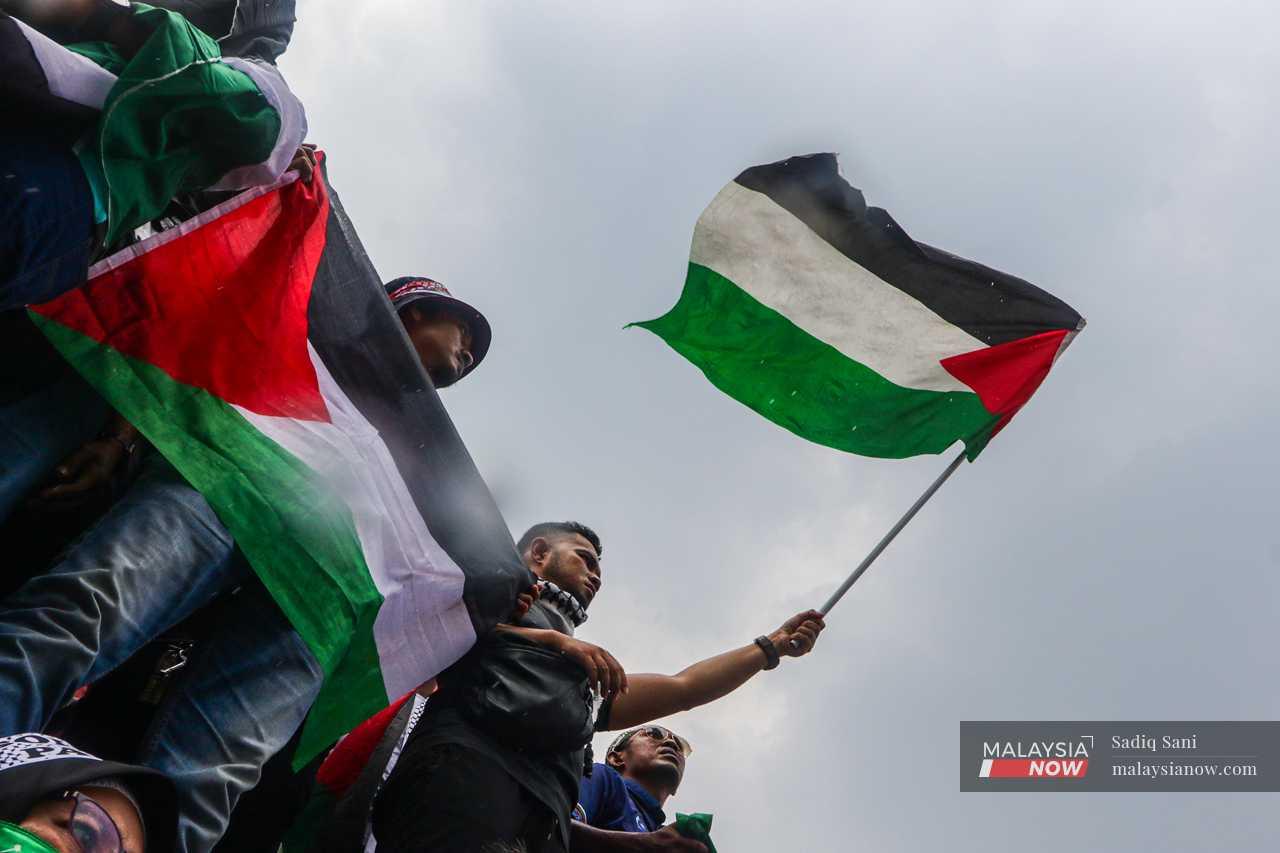 A group of youths wave Palestinian flags at oncoming traffic outside the US embassy in Jalan Tun Razak.
