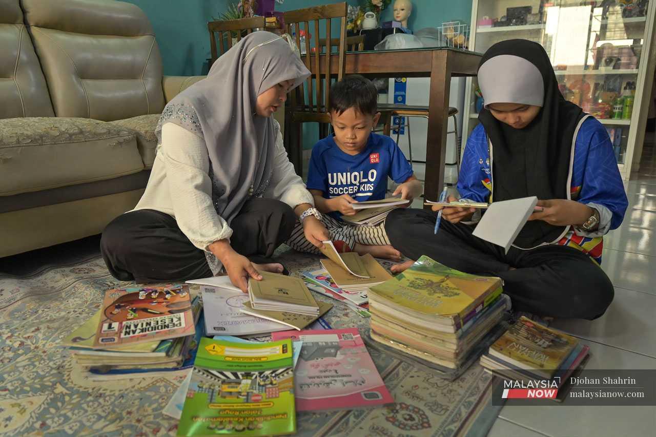 Suri rumah Mariam Hassan, 42, menyusun buku sekolah bersama anak-anaknya, Nur Aisyah Mohd Affian, 14, dan Aus Ikhwan, 7. Buku teks dipinjam dari sekolah tetapi buku latihan adalah baru, dibeli menggunakan wang simpanannya. Mariam memperuntukkan kira-kira RM500 setiap seorang untuk menampung kos keperluan sekolah dan pakaian seragam.