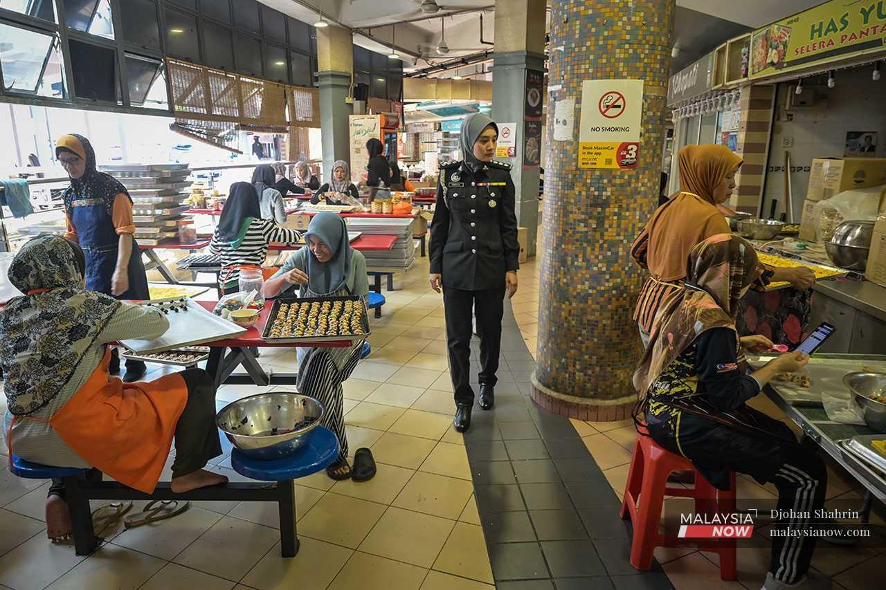 At a food court at Keramat Mall, an officer patrols the area as workers hurry to prepare all of the biscuits and kuih that they need to meet the orders placed by customers ahead of the Hari Raya celebration.
