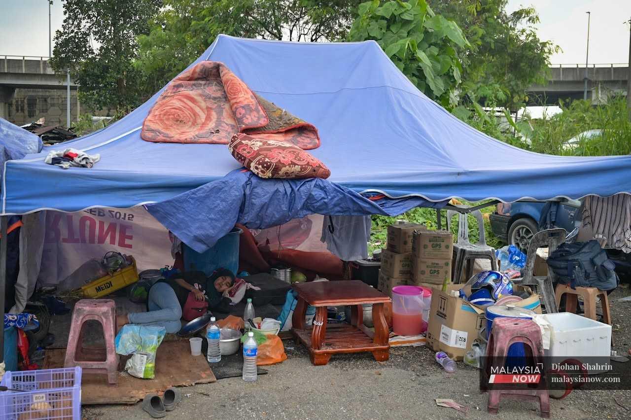 A resident of Kampung Sri Makmur takes a nap under a tent surrounded by the belongings she saved after her house was demolished by authorities on May 27, 2024.