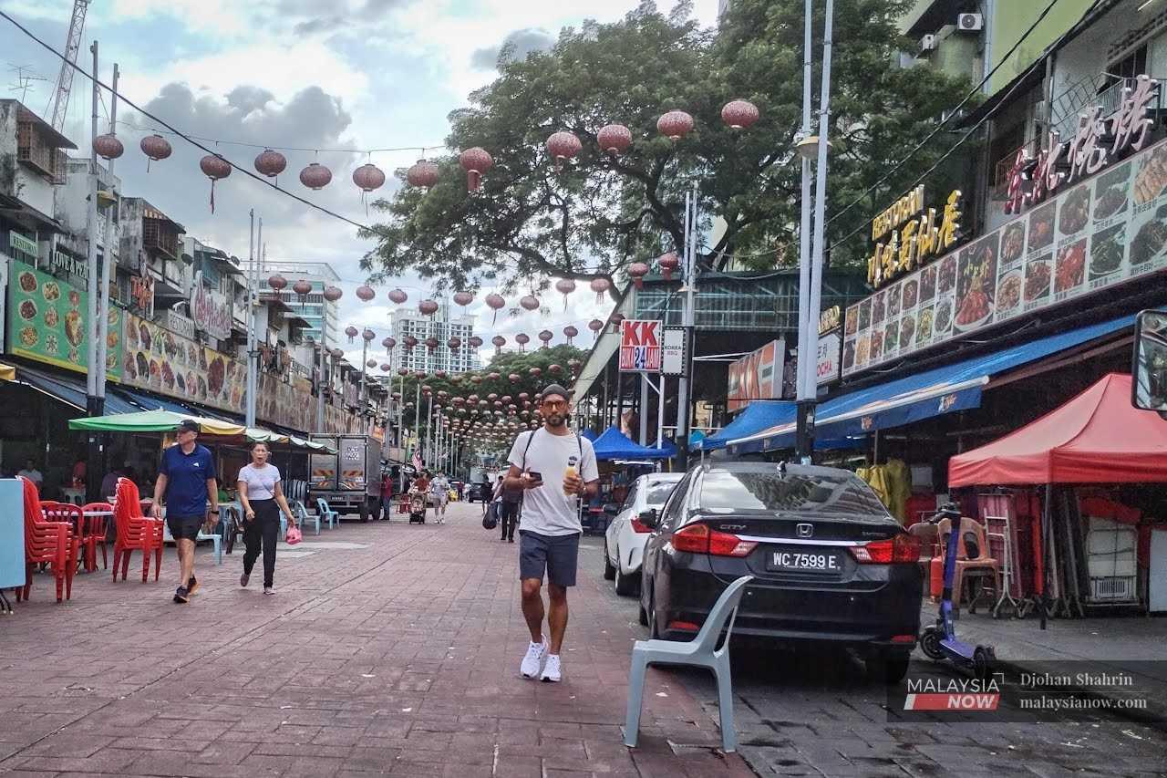 Pelancong berjalan di hadapan restoran memaparkan papan tanda yang mengutamakan bahasa selain Bahasa Melayu di Jalan Alor, Bukit Bintang.