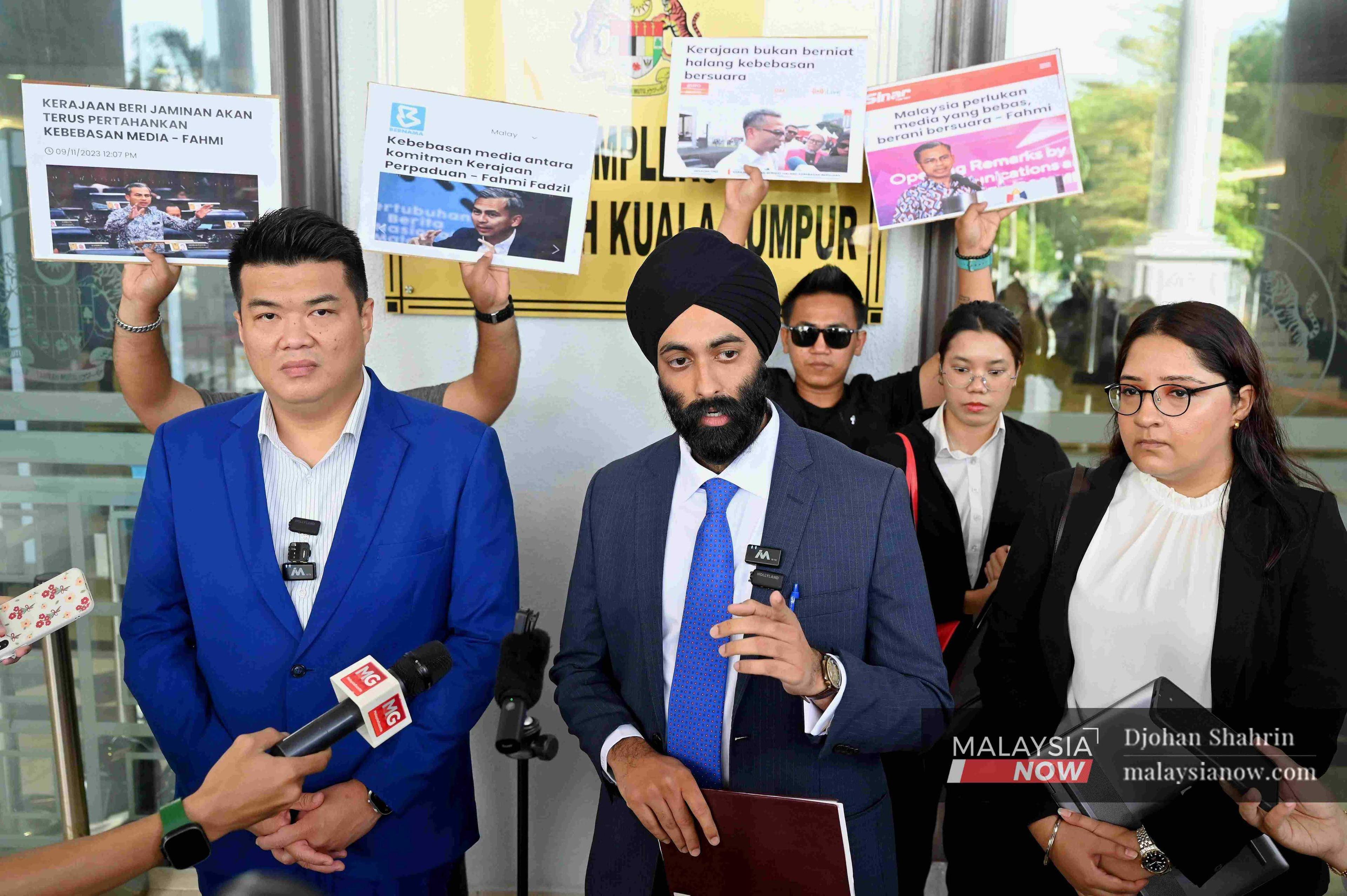 Activists hold placards displaying past news reports quoting Communications Minister Fahmi Fadzil's pledge to protect free speech, during a press conference by Albert Tei and his lawyer, Mahajoth Singh.