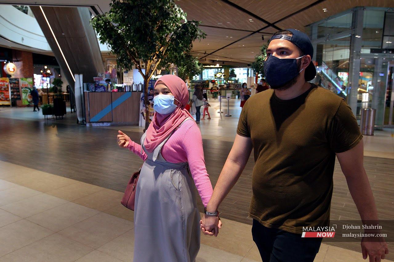 Sepasang suami isteri berjalan berpimpin tangan di sebuah kompleks membeli belah di Shah Alam, Selangor. Gambar: MalaysiaNow