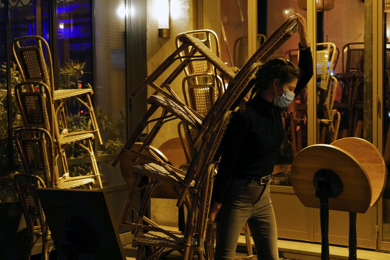 A waiter carries chairs to close a bar terrace in Paris. Photo: AP