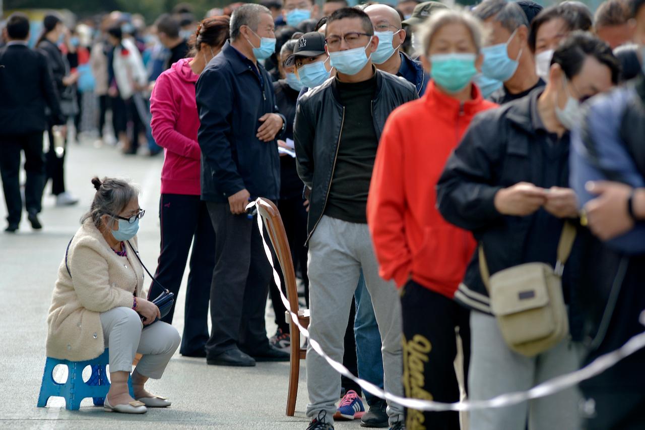 A woman wearing a face mask to help curb the spread of the coronavirus sits on a stool as residents line up to be tested for Covid-19 near the residential area in Qingdao in east China's Shandong province on Oct 12. Photo: AP